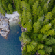 An aerial capture of Vernon Bay, with shining blue water surrounded by craggy rocks on the left bordered by lush green old-growth treetops.