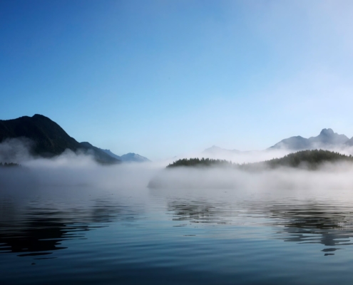 Morning mist hangs over Clayoquot Sound with mountains in the background.